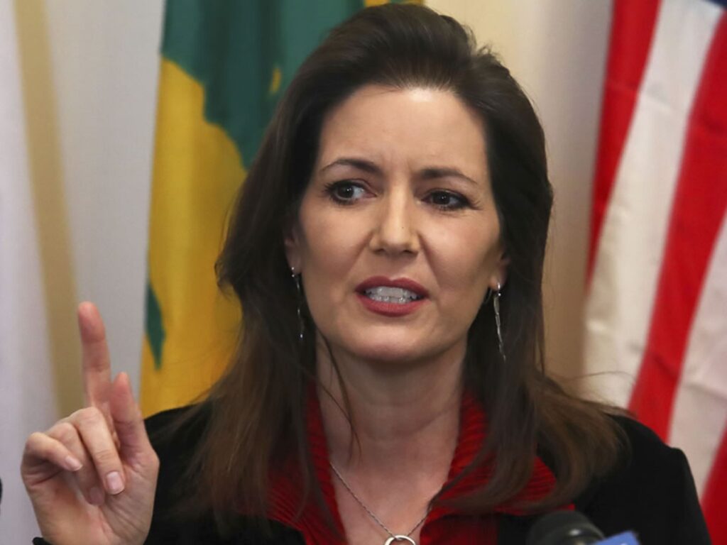 Oakland Mayor Libby Schaaf standing at podium in front of flags